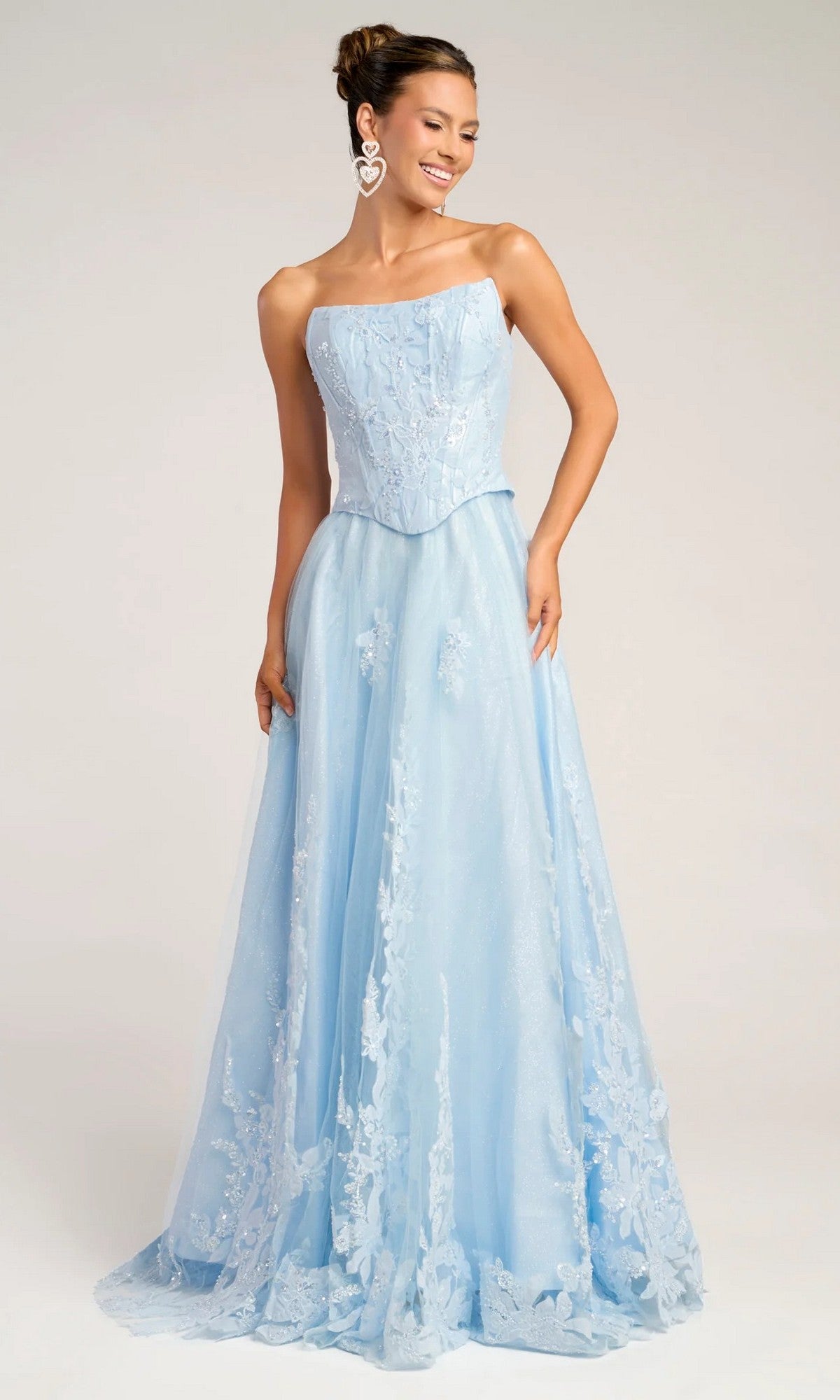 A woman stands and smiles in the Portia and Scarlett PS26061 long formal blue dress, featuring an A-line silhouette, a strapless corset bodice, and floral lace details against a neutral backdrop.